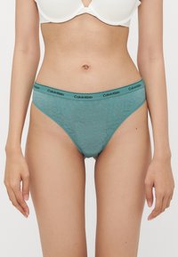 Teal kanten slipjes met een logo band in zwart. De stof heeft een bloemenpatroon en een lage taille. Zachte textuur, ontworpen voor comfort.