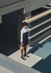 Robe bicolore marine et blanche de style chemise col, associée à des collants noirs et des chaussures noir et blanc, sur fond de béton.