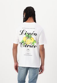 Hvid bomulds t-shirt med et farverigt citron grafik og tekst på ryggen, med en afslappet pasform og korte ærmer.