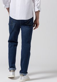 Jeans blu scuro con taglio dritto, caratterizzati da un design a yoke sulle tasche posteriori. Indossati con sneakers bianche e con i polsini arrotolati.