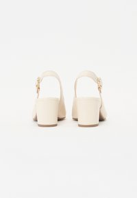 Beige slingback kengät, joissa on pyöristetyt varpaat ja keskipitkä lohko korko. Ominaisuuksiin kuuluu solkiyksityiskohta ja sileä nahkamaista tekstuuria.