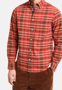 Camicia a quadri rossa con bottoni bianchi piccoli, con accenti verdi e marroni, realizzata in tessuto con finitura testurizzata.