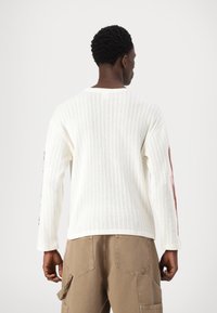 Maglione bianco a maglia con una vestibilità morbida, caratterizzato da maniche lunghe e un motivo testurizzato, abbinato a pantaloni cargo beige.