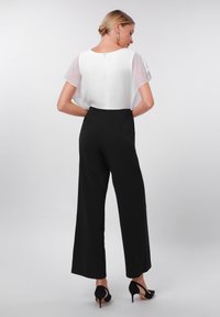 Black wide-leg trousers paired with a sheer white blouse, featuring short sleeves and a keyhole back closure. Black high-heeled shoes.