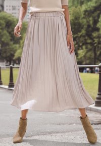 Gonna maxi plissettata di un leggero beige, realizzata in un tessuto morbido, con una vita elastica e un design fluido, abbinata a stivaletti alla caviglia color nocciola.