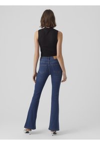 Pantalones vaqueros acampanados de color azul con una cintura alta, hechos de tela de mezclilla. Presenta dos bolsillos traseros y una etiqueta de cuero marrón en la cinturilla.