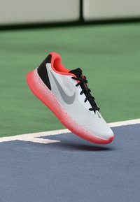 Weißer Sportschuh mit grauem Nike-Logo, schwarzen Akzenten und einer rosafarbenen, gesprenkelten Sohle, entwickelt für Leistung auf Hallenböden.