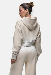 Sweat à capuche beige raccourci avec des manches oversized et des poignets côtelés. Texture douce avec un léger dégradé vers l'ourlet.