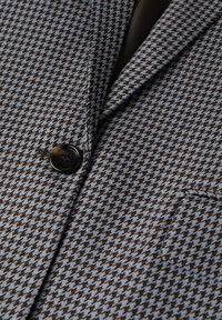 Brązowa i niebieska marynarka w kratę houndstooth z klapką, pojedynczym zapięciem na guzik i teksturowanym materiałem. Posiada kieszeń na piersi.