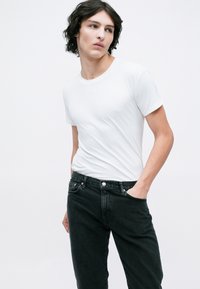 Hvid crew-neck t-shirt i et blødt og glat stof, parret med højtrækkende sorte denim jeans. Pasformen er afslappet med minimal detaljering.