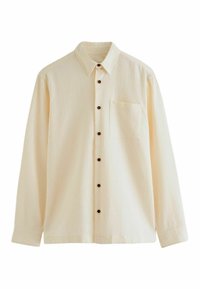 Chemise à manches longues, couleur crème, avec un motif texturé en gaufre, un devant à boutons et une poche poitrine unique. Les boutons marron contrastent avec le tissu.