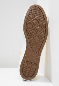 Baskets blanches avec une semelle extérieure en caoutchouc brun texturée présentant des motifs géométriques et un accent latéral jaune. Tige en textile lisse.