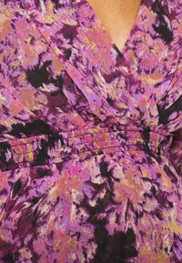 Tecido estampado em roxo e rosa com uma cintura franzida, apresentando um design de decote em V profundo e um material fluido texturizado.