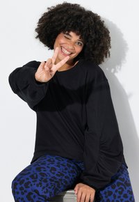 Top negro de manga larga con mangas fruncidas, combinado con leggings de estampado de leopardo azul. La modelo está sentada mientras hace una señal de paz.
