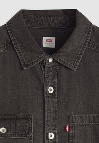 Chemise en denim noir avec col, patte de boutonnage à l'avant et poche poitrine gauche. Dotée de boutons argentés et d'une étiquette rouge Levi's sur la poche.