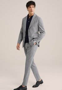 Lichtgrijs geruit pak met een getailleerde pasvorm, gecombineerd met een marineblauwe polo. Voorzien van stijlvolle zwarte schoenen. Gladde textuur, modern ontwerp.