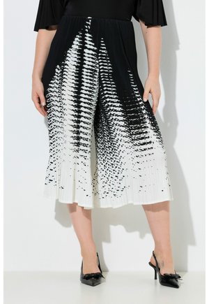 Donna che indossa pantaloni larghi plissettati a fantasia astratta in bianco e nero e tacchi neri a punta con fiocchi.