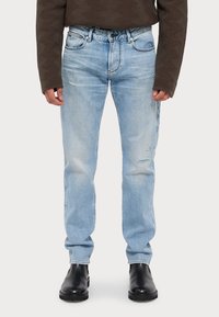 Light blue denim jeans with distressed detailing, straight-leg design, and a five-pocket style, paired with black ankle boots.