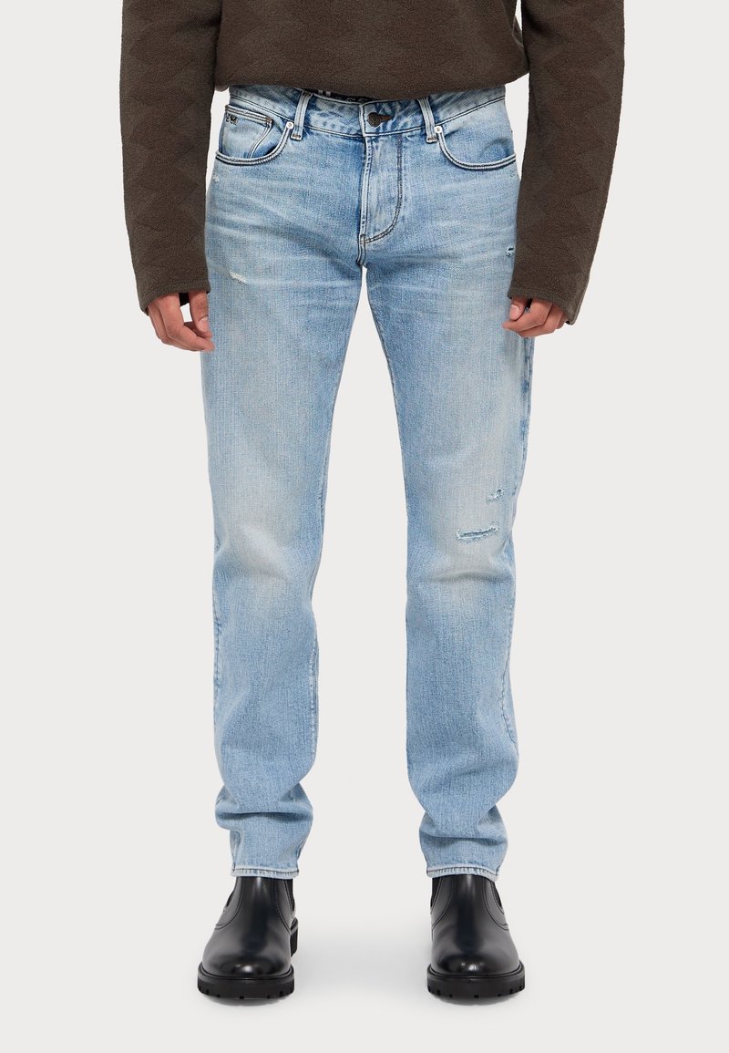 Light blue denim jeans with distressed detailing, straight-leg design, and a five-pocket style, paired with black ankle boots.