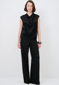 Top in satin nero con scollatura drappeggiata, abbinato a pantaloni neri a vita alta e pantaloni larghi. Accessoriato con un bracciale trasparente e un bracciale nero.