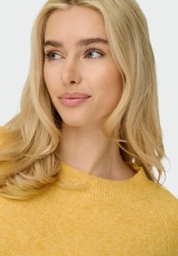 Yellow textured sweater with a ribbed neckline, featuring a relaxed fit and soft fibers, worn by a model with long blonde hair.
