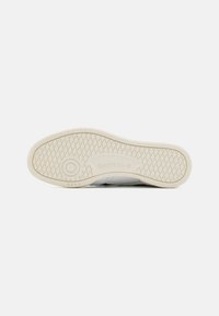 Valge spordijalatsite tallaga, millel on tekstureeritud kummipind, ringikujuline detail ja Reebok bränding keskosas.