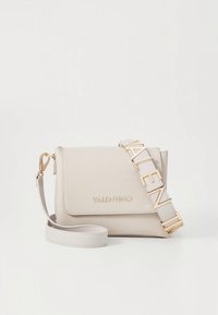 Τσάντα χειρός από ανοιχτό μπεζ δέρμα με μπροστινό καπάκι, χρυσή λεπτομέρεια με το λογότυπο και φαρδιά ράβδο με το όνομα της μάρκας σε κεφαλαία γράμματα.