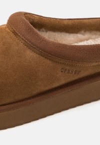 Brūni zamšādas slip-on apavi ar mīkstu iekšējo oderi, mīkstinātu apkakli un teksturētu zoli. Sānos ir iepresēta uzraksts.