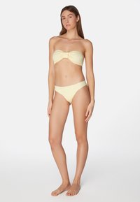 Gul texturerad bandeau-bikinitopp med knutdetalj, tillsammans med matchande lågrisk bikinibyxor. Slät tyg och minimalistisk design.