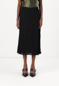 Svart plisse midi skjørt med elastisk midjebånd, parret med svarte pumps med spiss tå og sølvspenne. Glatt stofftekstur.