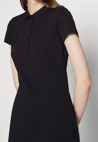 Polo noir avec un col classique et des manches courtes. Comprend une patte de boutonnage et un logo brodé discret sur la poitrine gauche.