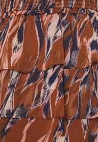 Tela de tonos marrón y rosa en capas con un patrón abstracto. Material ligero que presenta bordes con volantes y una textura suave.