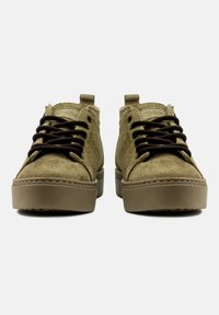 Kakifärgade mockaskor med bruna snören, låg ankeldesign och en platt gummisula. Har en stickad kant längs sulan.