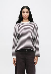 Μπλούζα με μακριά μανίκια σε ρίγες βουργουνδί και λευκό, με στρογγυλή λαιμόκοψη και μικρό λογότυπο στο στήθος. Συνδυασμένη με σκούρο παντελόνι.