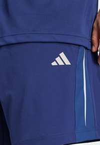 Pantalones cortos deportivos de Adidas en azul oscuro, con un logo blanco, panel lateral texturizado y acentos en azul claro. Fabricados con material ligero y transpirable.