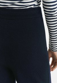 Persoon in marineblauwe gebreide broek en een zwart-witte gestreepte lange mouw shirt, waarbij de achterkant van de taille en de rechterarm zichtbaar zijn.