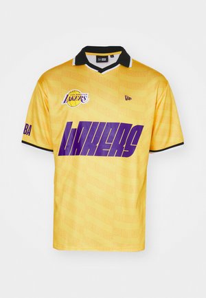 Canotta da basket gialla con colletto nero, caratterizzata da grande testo e logo "LAKERS" viola, realizzata in tessuto morbido con uno sfondo a motivo sottile.