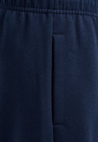 Granatowe dresy o miękkiej fakturze, z elastycznym pasem i boczną kieszenią. Tkanina ma gładki, równomierny wzór dzianiny.