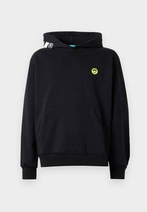 Felpa nera con tasca frontale, faccina sorridente verde neon con zanne sul petto e dettaglio logo bianco sul lato sinistro del cappuccio.