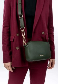 Borsa a tracolla verde in pelle con superficie testurizzata, forma rettangolare, accessori in metallo dorato e tracolla regolabile. Decorata con un logo.