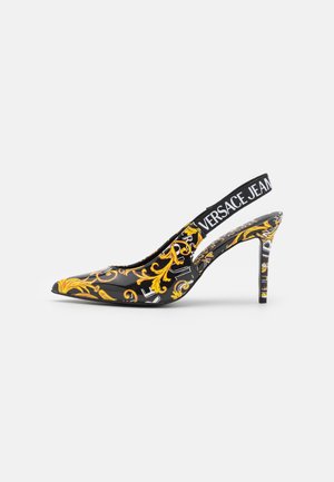 Czarny lakierowany but na wysokim obcasie typu slingback z żółtym wzorem barokowym i elastycznym paskiem z napisem „VERSACE JEANS”.