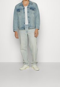 Ljust blå denimjacka med två bröstfickor, matchad med ljusblå raka jeans och vita sneakers. Enkelt design och avslappnad passform.