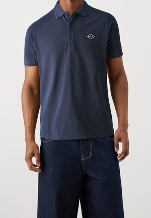 Polo shirt blu navy in cotone, con colletto, tre bottoni e una piccola toppa con logo bianco sul lato sinistro del petto.