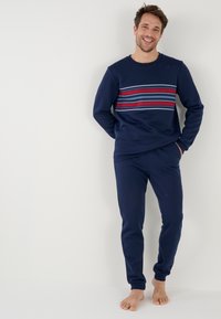 Marineblauwe sweatshirt en broeken set met horizontale strepen in rood, blauw en grijs. Glad stof met ronde halslijn en taps toelopende mouwen.