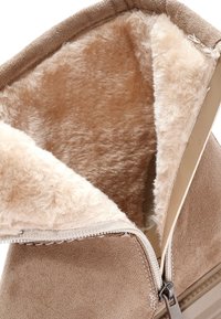 Bota de ante color beige con un suave forro de piel sintética. Cuenta con una cremallera lateral para un fácil acceso y un exterior suave y texturizado.