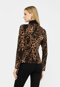 Top con stampa leopardata in marrone e nero, maniche lunghe, design aderente, texture liscia, con colletto nero e orlo dritto.