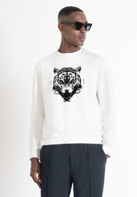 Sudadera blanca con un gráfico de tigre en negro y gris en la parte frontal, hecha de una suave tela de mezcla de algodón; combinada con pantalones oscuros.