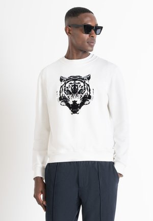 Sudadera blanca con un gráfico de tigre en negro y gris en la parte frontal, hecha de una suave tela de mezcla de algodón; combinada con pantalones oscuros.