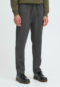 Szare spodnie z elastycznym pasem, dopasowane, wykonane z miękkiego materiału, z bocznymi kieszeniami i sznurkiem. W połączeniu z czarnymi butami typu lace-up.