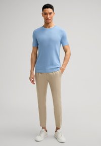 Maglione a maglia corto azzurro chiaro, pantaloni beige affusolati e sneakers bianche. Design semplice con una maglia testurizzata e una palette di colori neutri.